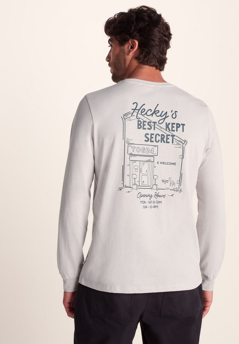 Long-sleeve light gray shirt featuring a graphic print on the back. Graphic shows a building and text elements outlining business info.