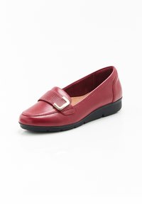 Scarpa slip-on rossa in pelle con suola nera bassa in gomma, dotata di una cinghia testurizzata e di dettagli in tono oro sulla parte superiore.