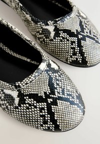 Sort-hvide flade sko med slangeskindsprint, glat tekstur, rundet tå og elastisk åbning for nem påtagning.