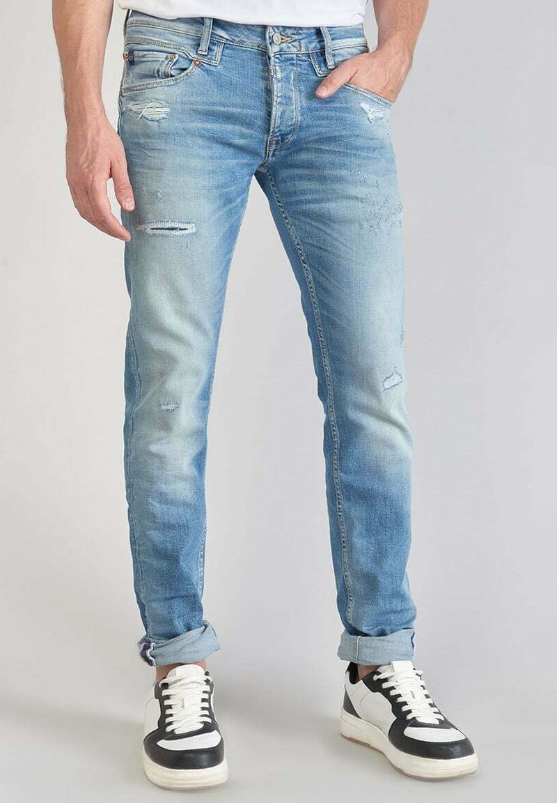 Lichtblauwe denim jeans met een slim fit, voorzien van versleten details en een vervaagde textuur. Gepaard met zwart-witte sneakers.