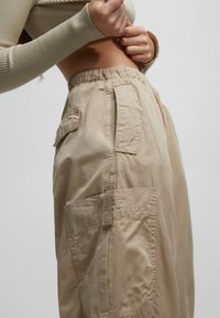 Beige cargobroek met een losse pasvorm, voorzien van een elastische tailleband, meerdere zakken en een zachte, gestructureerde stof.