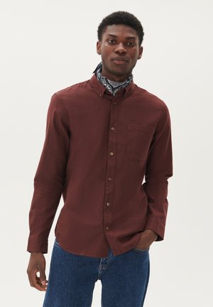 Bordeaux langærmet skjorte med knap-om-krave, enkelt brystlomme og brune knapper; båret med et mønstret blåt tørklæde og denimjeans.