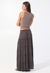 Top en tricot marron associé à une longue jupe maxi à volants en tissu léger et doux, avec une ceinture élastique confortable.