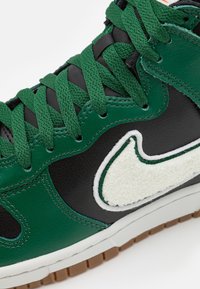 Zapatillas de cuero verde con detalles en negro, presentando un swoosh texturizado en color crema, suela de goma estriada y cordones verdes.