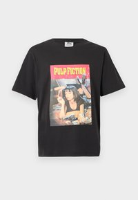 Μαύρο T-shirt με γραφικό μιας γυναίκας που ξαπλώνει σε ένα κρεβάτι κρατώντας έναν αναπτήρα, ένα πιστόλι στο κρεβάτι, και το κείμενο "PULP FICTION" από πάνω.