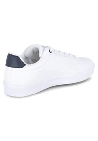 Zapatilla blanca con un upper de cuero liso, presentando un refuerzo en el talón de color azul marino, suela de goma blanca plana y seis ojales para los cordones.