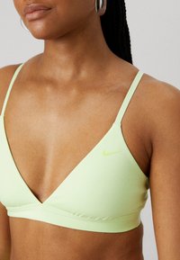 Bralette de sport vert clair en tissu lisse, avec un design à deep V et un petit logo Nike blanc sur le côté gauche.