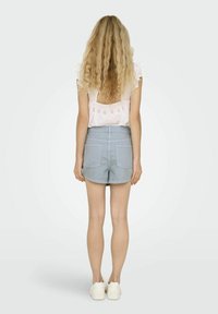 Blouse brodée rose clair à manches courtes ; shorts en coton bleu clair ; baskets blanches ; vue de dos sur un fond neutre.