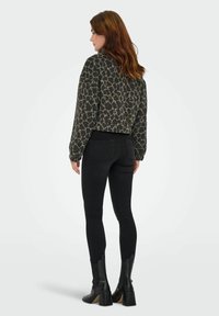 Korte, leopardenprint top in donkergrijs en zwart, gecombineerd met zwarte skinny jeans en enkellaarsjes met hak in zwart. Gegevens van de textuur van de stof.