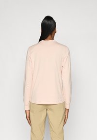 Lichtroze long-sleeve t-shirt met een ronde hals en geribbelde manchetten, gemaakt van zachte stof, gezien van de achterkant tegen een effen achtergrond.