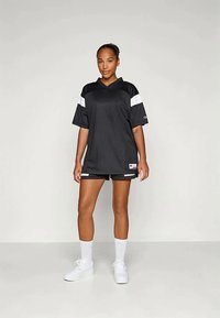 Črno športno majico z belimi črtami na rokavih, kombinirano s črnimi kratkimi hlačami. Kratki rokavi, ohlapen kroj in material, ki odganja vlago. Bele superge in nogavice.