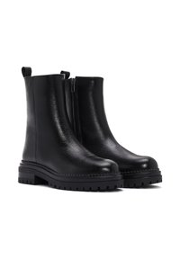 Botas de tobillo de cuero negro con un acabado texturizado, cremallera lateral y suela de goma gruesa. Asa en el talón para facilitar su uso.