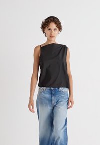 Top sans manches noir avec un décolleté asymétrique, fabriqué en tissu lisse, associé à un jean baggy bleu clair.