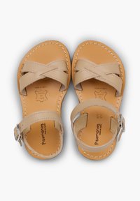 Beige nahka sandaalit, joissa on ristikkäiset hihnat ja nilkkahihna, jossa on solki. Näkyvissä on teksturoitu pohjallinen ja ompeluyksityiskohtia.