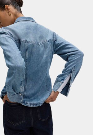 Jasnoniebieska dżinsowa kurtka o dopasowanym kroju, z zatrzaskami, spiczastym kołnierzem i podwiniętymi rękawami z białymi akcentami.