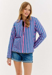 Kurtka pikowana w odważne pionowe paski w kolorze różowym i niebieskim. Posiada stójkę i zamek błyskawiczny z przodu. Połączona z dżinsowymi szortami.