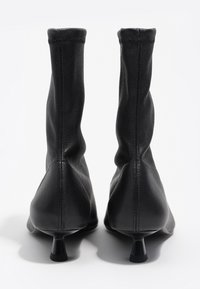 Czarne botki na kostkę z miękkim, teksturowanym wykończeniem z imitacji skóry, charakteryzujące się zwężanym kształtem noska i smukłym, niskim obcasem dla dopasowanej sylwetki.