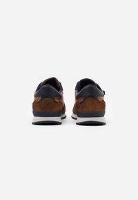 Brown suede and navy leather sneakers with a white midsole and textured black outsole. Rounded design, padded collar, and pull tab detail.