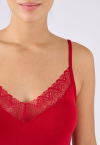 Top rosso senza maniche con un collo in pizzo. Il tessuto è liscio e aderente, con spalline sottili e un design a V.