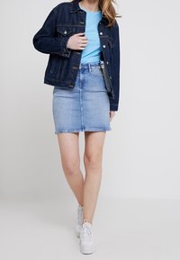 Jeansjacka i mörkblått, ljusblå t-shirt och en ljus denimkjol, kombinerad med vita sneakers. Har en klassisk denimdesign med knappstängningar.