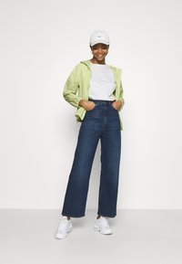 Svetlo zelena zip-up jakna, bela majica, temno modri široki jeans z visokim pasom, in bele superge, kombinirane z belo kapo.