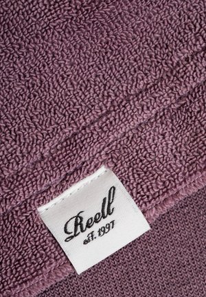 Purple towel with a textured surface, featuring a corner label that reads "Reell est. 1991" on a white fabric tag.