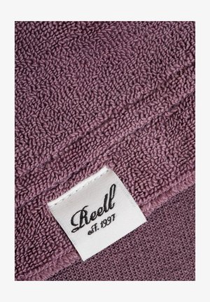 Purple towel with a textured surface, featuring a corner label that reads "Reell est. 1991" on a white fabric tag.