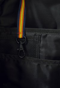 Schwarzes Stoffinterieur mit einer Netztasche, einem schwarzen Clip-Haken und einem bunten gestreiften Gurt in Blau, Gelb und Rot.