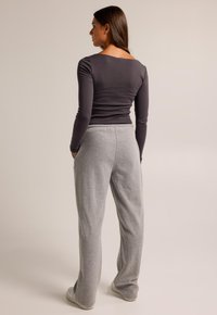 Pantalons de jogging gris à coupe décontractée, dotés de poches latérales, associés à un haut à manches longues gris foncé ajusté ; matière en coton douce.