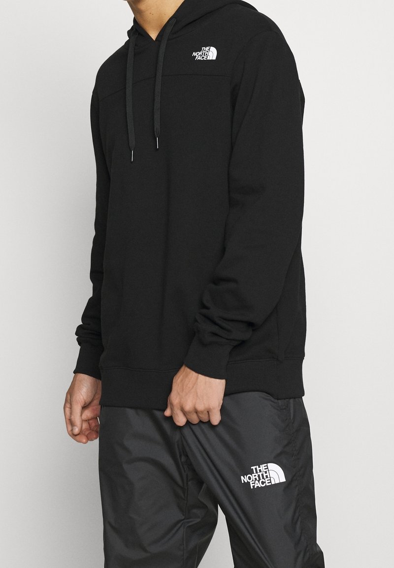 Black hoodie with a drawstring, featuring a logo on the chest. Paired with gray, lightweight pants that have a matching logo on the thigh.