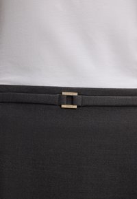 Tessuto grigio con una finitura liscia, caratterizzato da una parte superiore bianca e due dettagli in metallo dorato nella parte inferiore. Design minimalista, linee pulite.