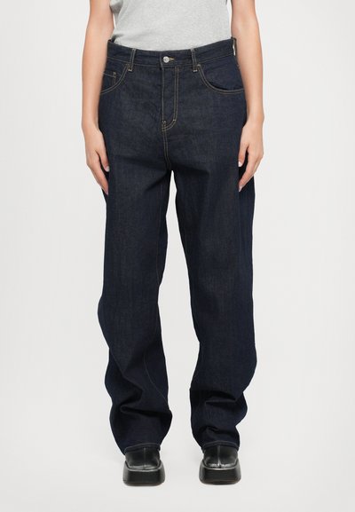 Jean en denim bleu foncé à coupe décontractée, avec des coutures dorées, cinq poches et une fermeture à bouton à la taille.