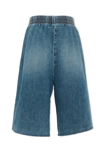 Shorts larges en denim bleu avec ceinture élastique froncée et légère décoloration sur les jambes, vus de face.