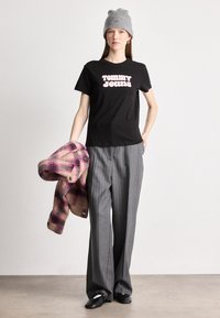 Μαύρη μπλούζα t-shirt με ροζ λογότυπο "TOMMY JEANS", γκρι παντελόνι με ρίγες και ροζ καρό ζακέτα. Γκρι σκουφάκι και μαύρα ανατομικά παπούτσια.