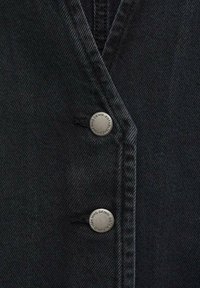 Sort denimjakke med vævet tekstur, med en dobbeltradet front og sølvknapper med indgraverede mærkedetaljer.