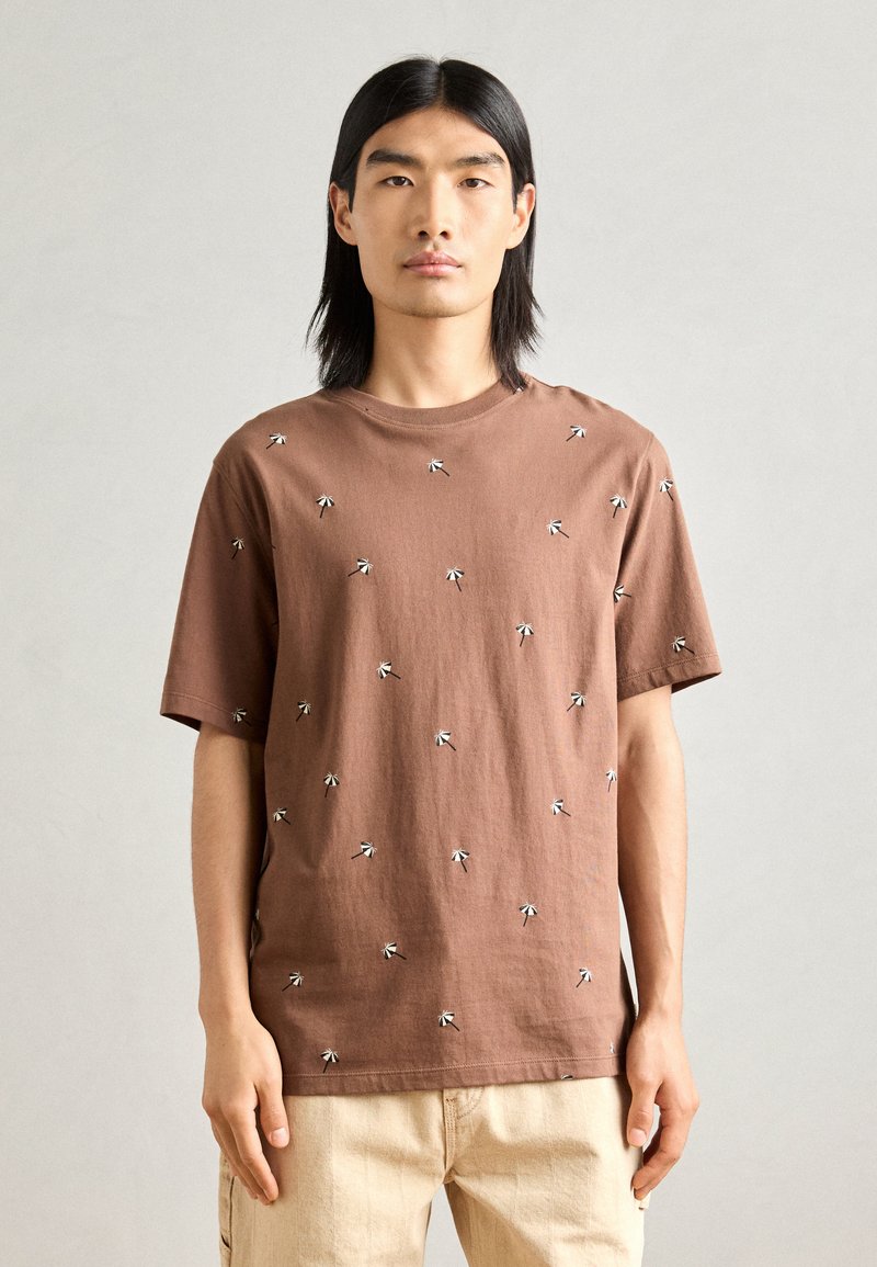Brun bomulds t-shirt med spredt hvid broderi, korte ærmer, rund hals og en afslappet pasform.