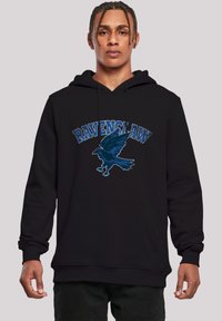 Svart hettegenser med et blått "Ravenclaw"-grafikk og et design av en flygende ravn. Inkluderer en frontlomme og ribbede cuffs.