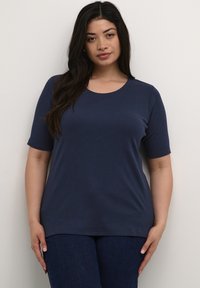 Camiseta de manga corta en azul marino, hecha de un tejido suave y elástico, con un cuello redondo y un corte holgado, combinada con jeans de mezclilla oscura.