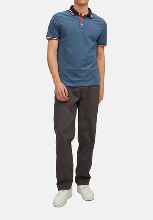 Polo bleu avec un col rayé rouge et bleu marine, manches courtes. Associé à un pantalon gris et des baskets blanches. Look décontracté.