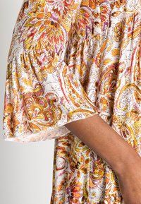 Kukkakuvioinen mekko, jossa on puffattuja lyhyitä hihoja, esittelee oransseja, keltaisia ja vaaleanpunaisia kuvioita valkoisella taustalla. Kevyt kangas.