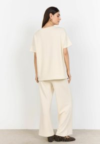 Cremefarvet loungewear-sæt med en løs top med korte ærmer og brede bukser. Glat tekstur, minimalistisk design og ingen synlige mønstre.
