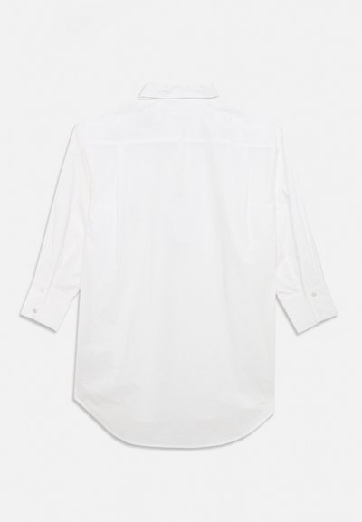Λευκό πουκάμισο με μακριά μανίκια, απλωμένο, που δείχνει την πίσω πλευρά, με κουμπωτά μανσέτα και κλασικό γιακά, σε απλό φωτεινό φόντο.