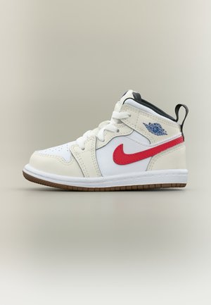 Baskets Air Jordan pour tout-petits blanches et beiges avec le swoosh Nike rouge, le logo Air Jordan bleu, un onglet à l’arrière noir et une semelle marron.