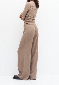 Haut beige en maille côtelée avec un design froncé, associé à un pantalon beige ample à jambes larges. Le matériau semble doux avec une texture subtile.