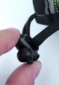 Schwarzer Kordelzugmechanismus, der zwischen den Fingern gehalten wird, mit einer runden Griffperle und geflochtenem Nylonband, dessen Oberfläche strukturiert ist, um einen besseren Halt zu bieten.