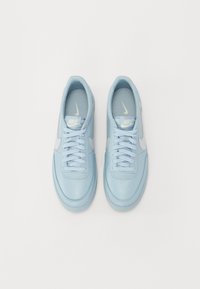 Heledsinine nahk-sneakerid tekstureeritud pindadega, lame pael ja valge Nike swoosh rõhuasetus. Minimalistlik disain, sujuv ümar nina.