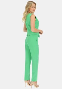 Zielony bezrękawnik z dekoltem w serek oraz dopasowane spodnie; obie części wykonane z gładkiego materiału. Posiada warstwowy detal na plecach i slim fit.