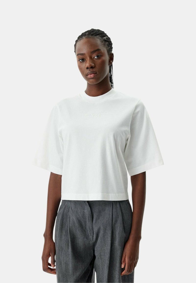 Witte cropped t-shirt met korte mouwen, met een subtiele "PINKO" logo in bijpassende draad. Zachte stof en een ontspannen pasvorm. Gecombineerd met grijze broeken.