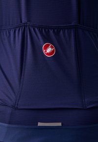Marineblaues Sportoberteil aus strukturiertem Stoff, mit einem roten runden Logo, auf dem ein weißer Skorpion abgebildet ist. Elastischer Saum zur Anpassung der Passform.