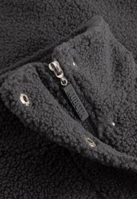 Szary fleecowy materiał o miękkiej, teksturowanej powierzchni. Posiada czarny suwak z etykietą "KUBOTA" oraz srebrne akcenty metalowe.